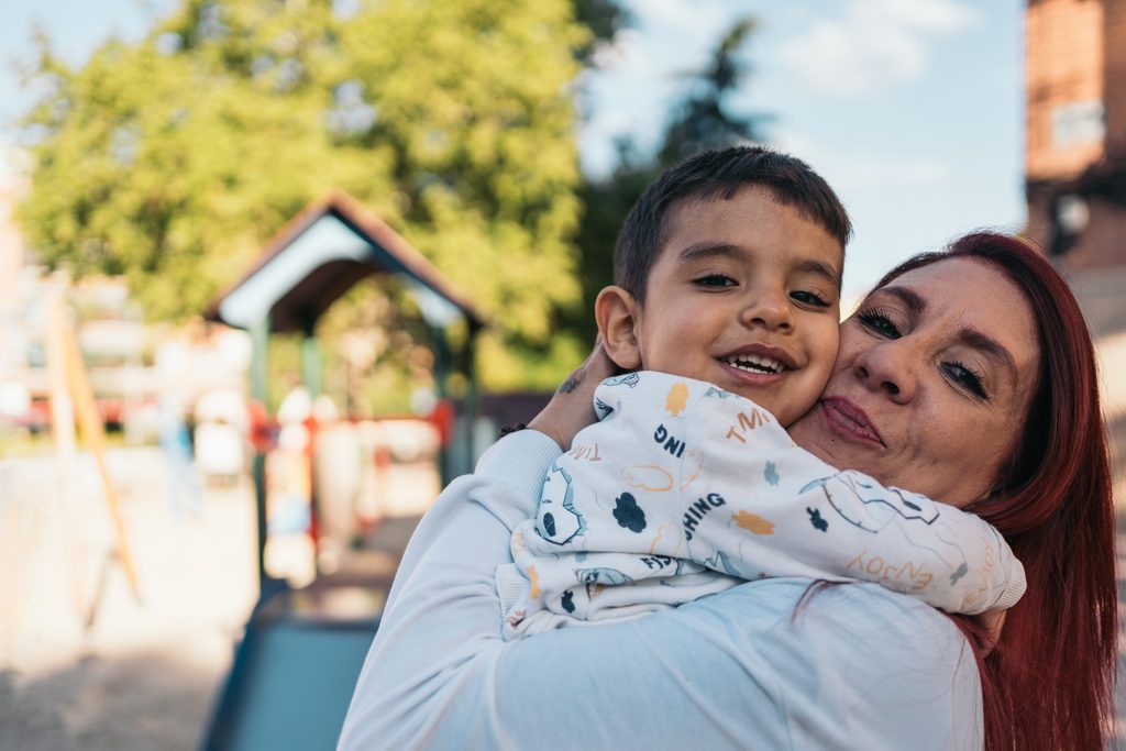 A parent and child embracing warmly at a playground.